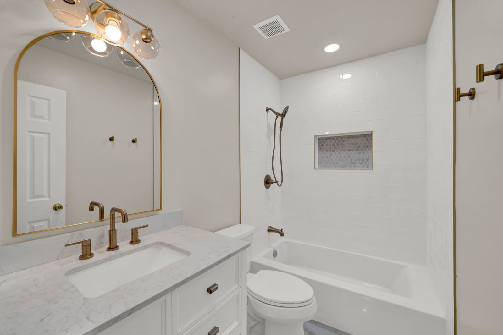A finished bathroom renovation by Garden State ADU: marble-look vanity, brushed-gold fixtures and a subway-tile tub surround.